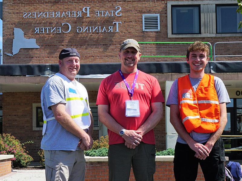 三名男子站在大楼前，并签署“国家备灾培训中心”。