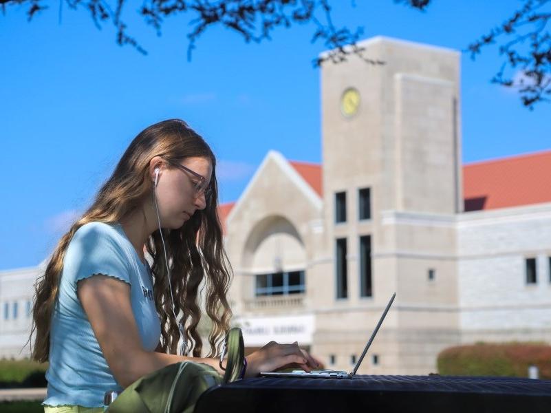 大学生坐在图书馆外，用笔记本电脑工作